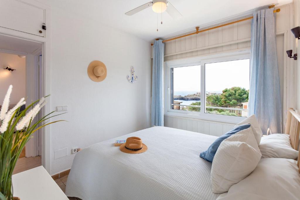 ein Schlafzimmer mit einem großen Fenster mit einem Hut auf einem Bett in der Unterkunft La Ola Beach House in Portocolom