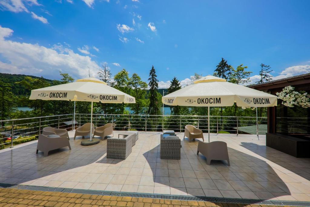 Sunny terrace with large OKOCIM umbrellas, modern lounge chairs and lake view.