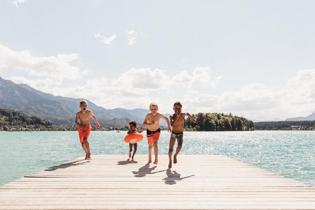 eine Gruppe von Menschen, die auf einem Dock im Wasser spazieren in der Unterkunft Naturel Hoteldorf Seeleitn in Faak am See