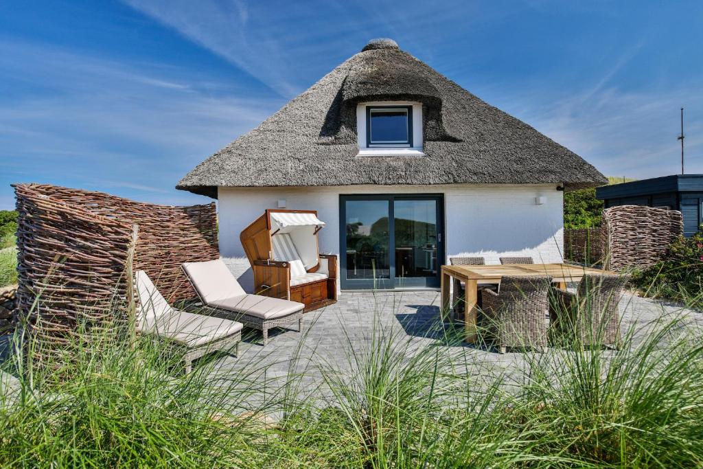 une maison au toit de chaume avec des chaises et une table dans l'établissement Strandhaus, à Hörnum