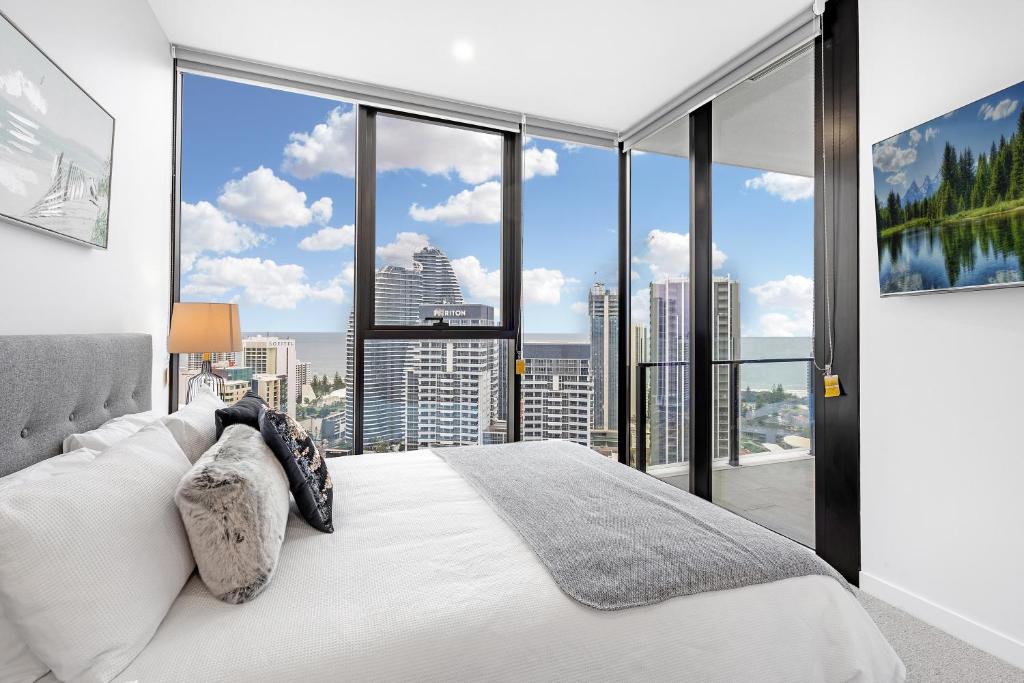 a bedroom with a white bed and large windows at Lamour Ocean View Apartment I in Casino Broadbeach - free parking in Gold Coast