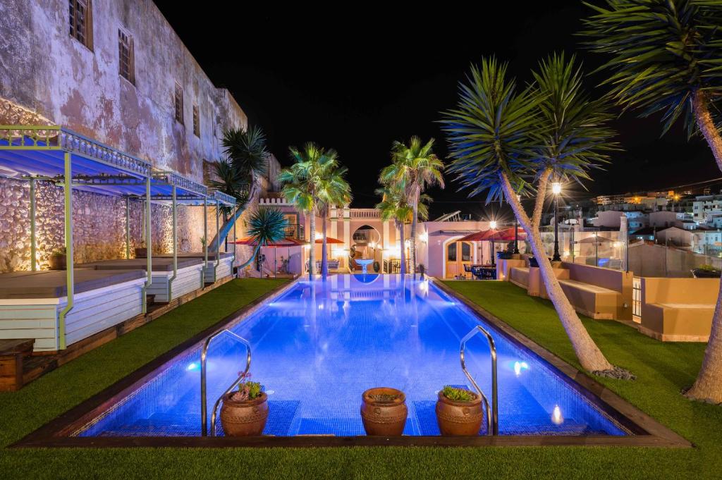 una piscina por la noche con palmeras y un edificio en Vila Origens Boutique Hotel Albufeira – Adults Only en Albufeira