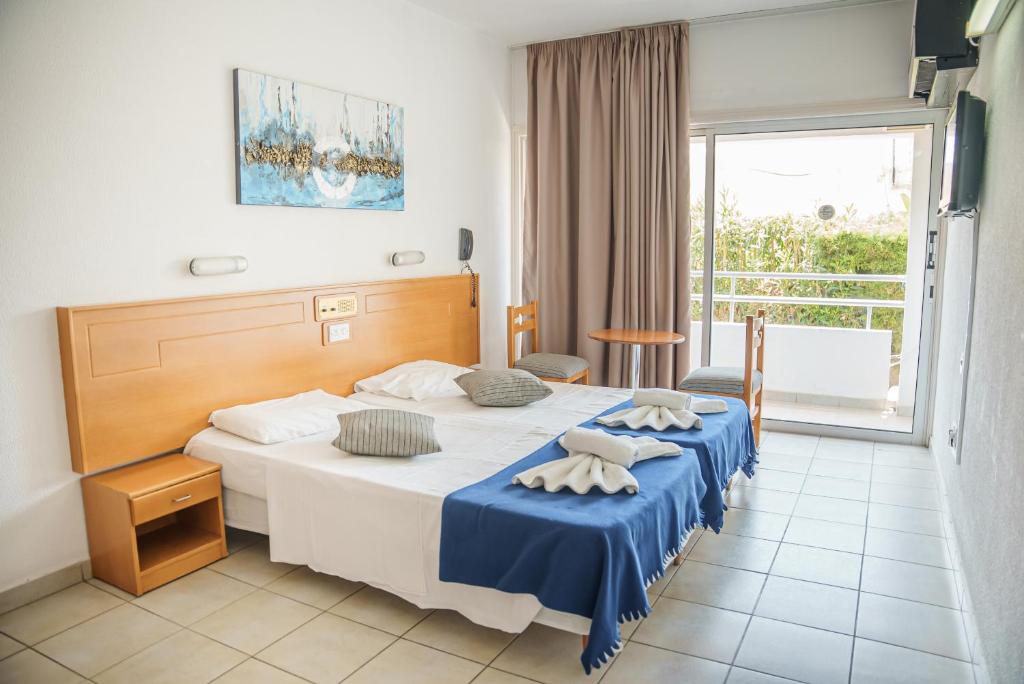 a hotel room with a bed with blue sheets and a window at Cornelia Hotel in Ayia Napa