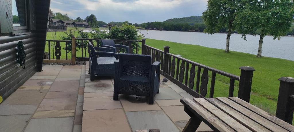 um alpendre com cadeiras e um banco ao lado de um lago em Tegid Lodge- Pine Lake Resort em Carnforth