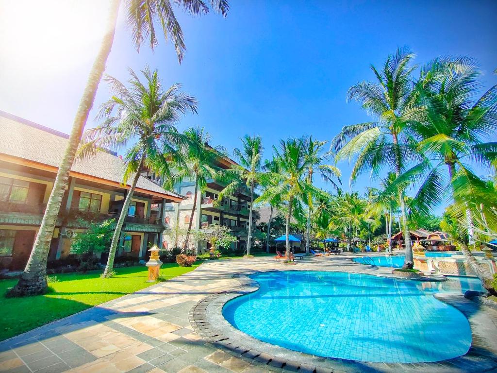 a resort swimming pool with palm trees and a fire hydrant at Jayakarta Hotel Lombok in Senggigi