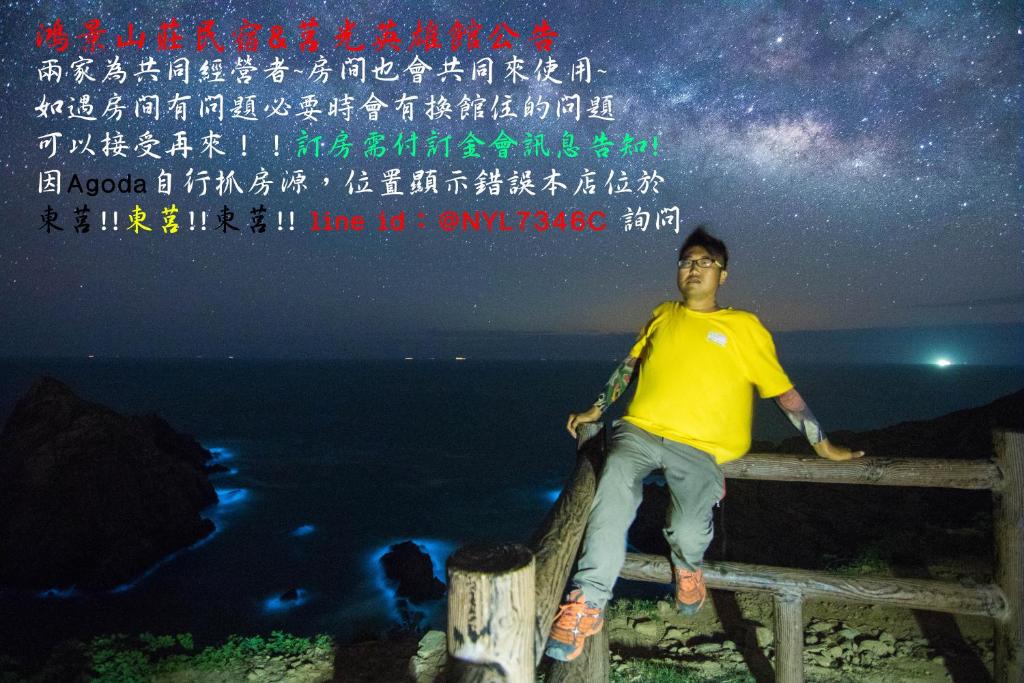Un uomo seduto su una recinzione sotto le stelle di 鴻景山莊民宿 b&B a Juguang