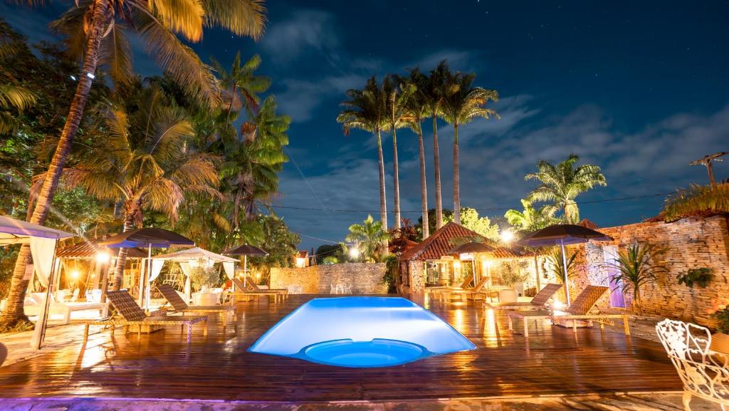 una piscina por la noche con palmeras y sombrillas en Pousada Villa das Pedras en Pirenópolis
