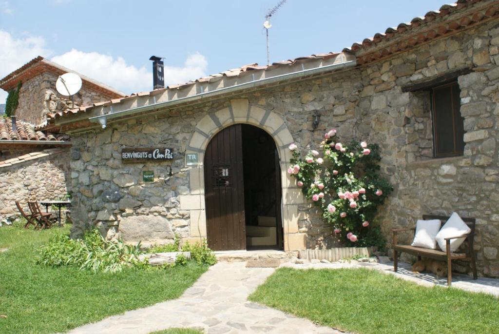 ein Steingebäude mit einer Tür und einem Busch mit Blumen in der Unterkunft Can Pei in Oix