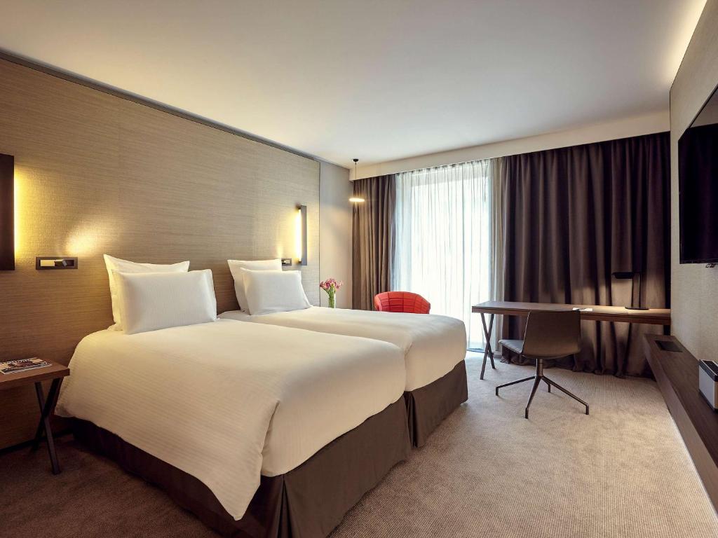 a hotel room with two beds and a television at Pullman Paris Roissy Cdg Airport in Roissy-en-France