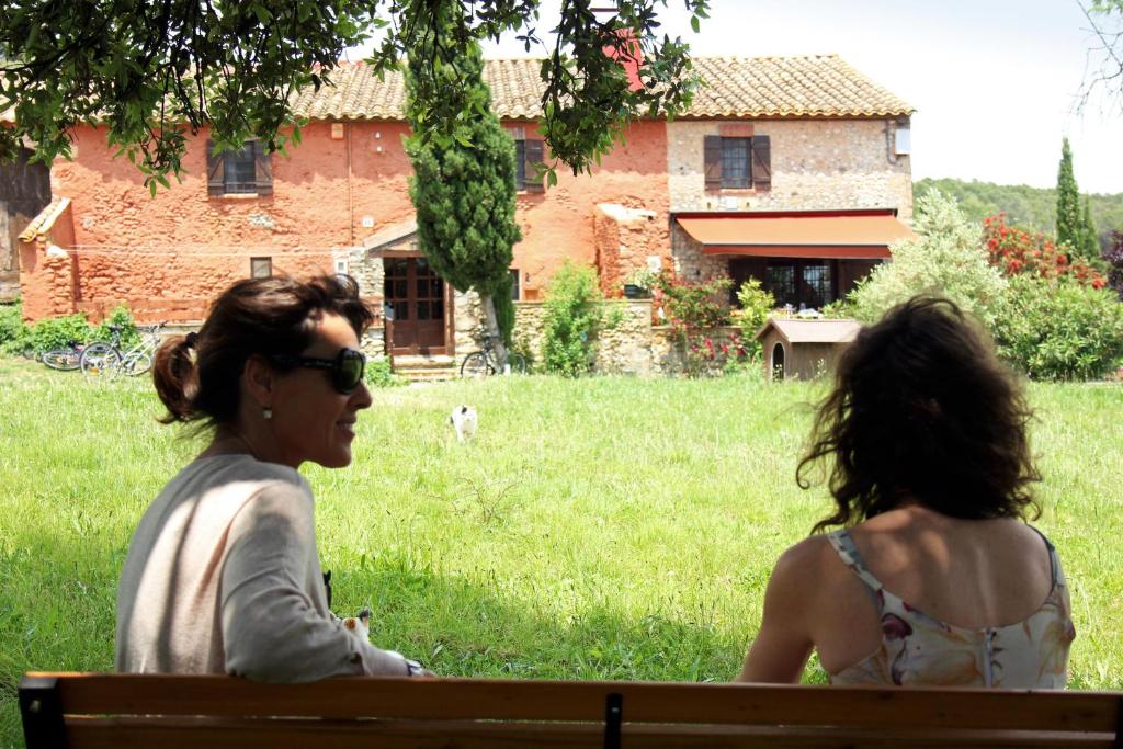 dos mujeres sentadas en un banco frente a un edificio en Mas La Casa Nova, en Pontós