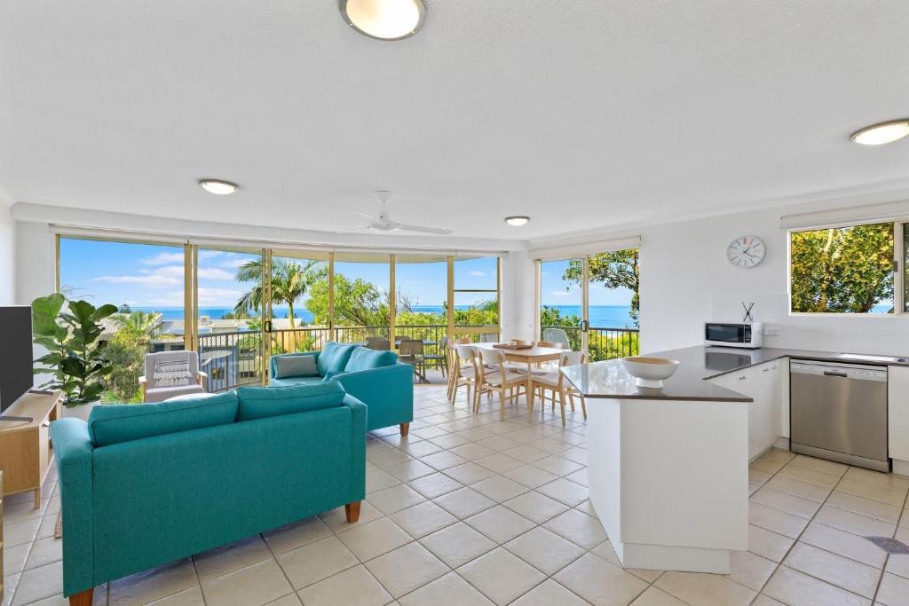 sala de estar con sofás azules y cocina en 6 Pacific Outlook Modern unit with lovely Ocean Views Pool in Complex Walk to Beach, en Sunshine Beach