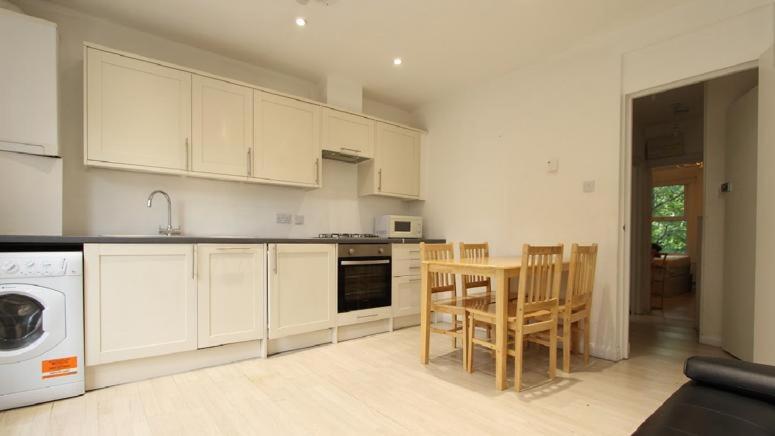cocina con armarios blancos, mesa y sillas en Cozy 4 Bed Flat in Islington London, en Londres