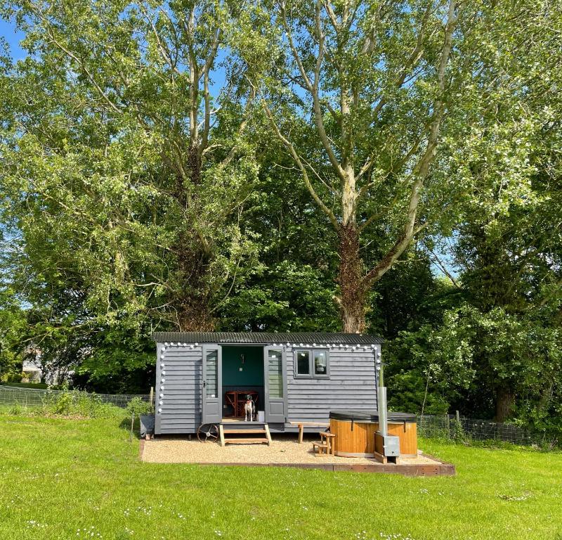 a small caravan in a field with a tree at Old King William Shepherd Huts and Private Hot Tubs in North Norfolk in Hunworth