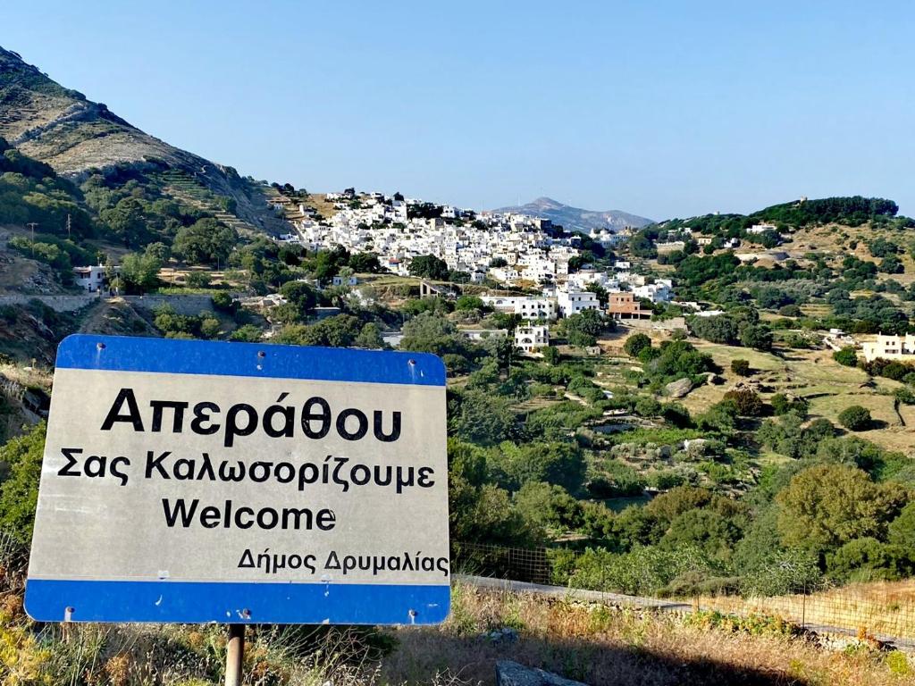 una señal en una colina con un pueblo en el fondo en On the road house en Apérathos