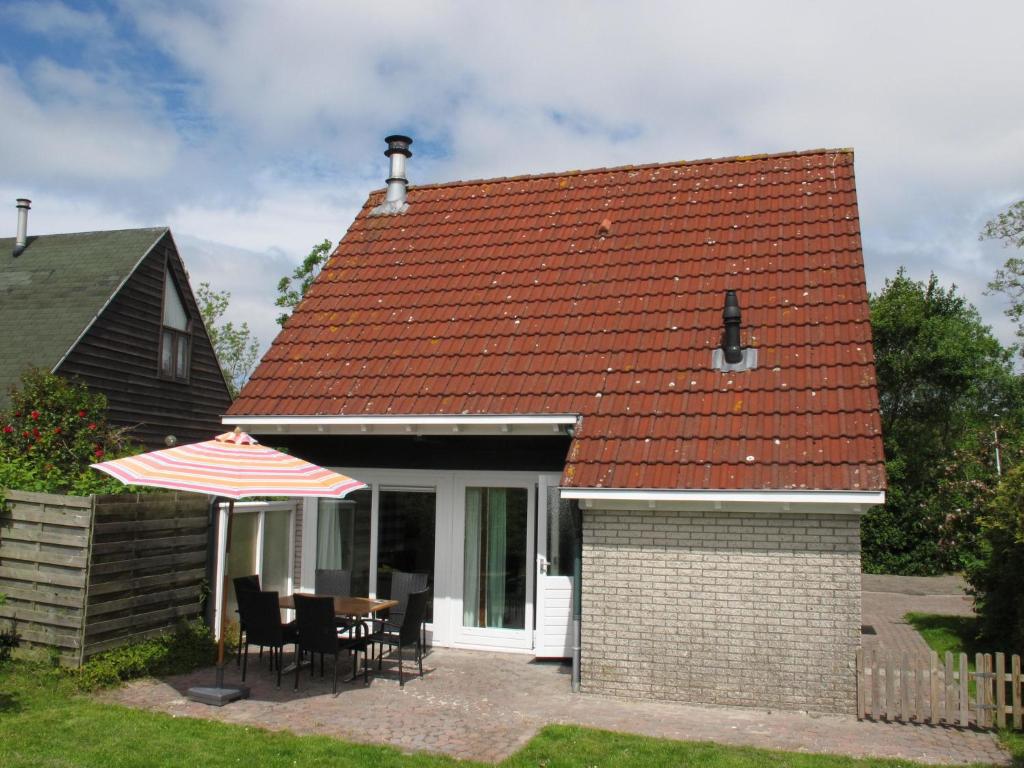 uma casa com uma mesa e cadeiras e um guarda-sol em Ferienhaus HET GANZELAND OOST100 em Oostmahorn