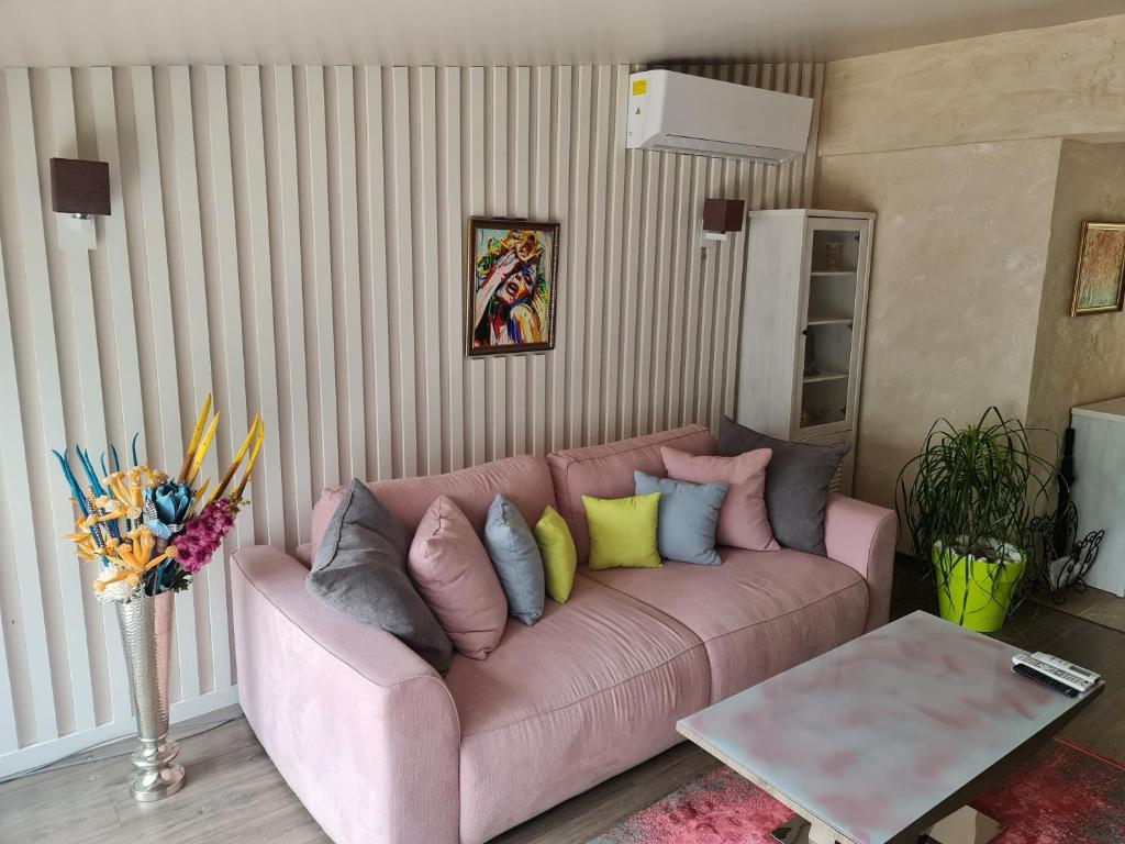 a living room with a pink couch with colorful pillows at GRANDE SPA DELUXe STUDIOS in Sliven