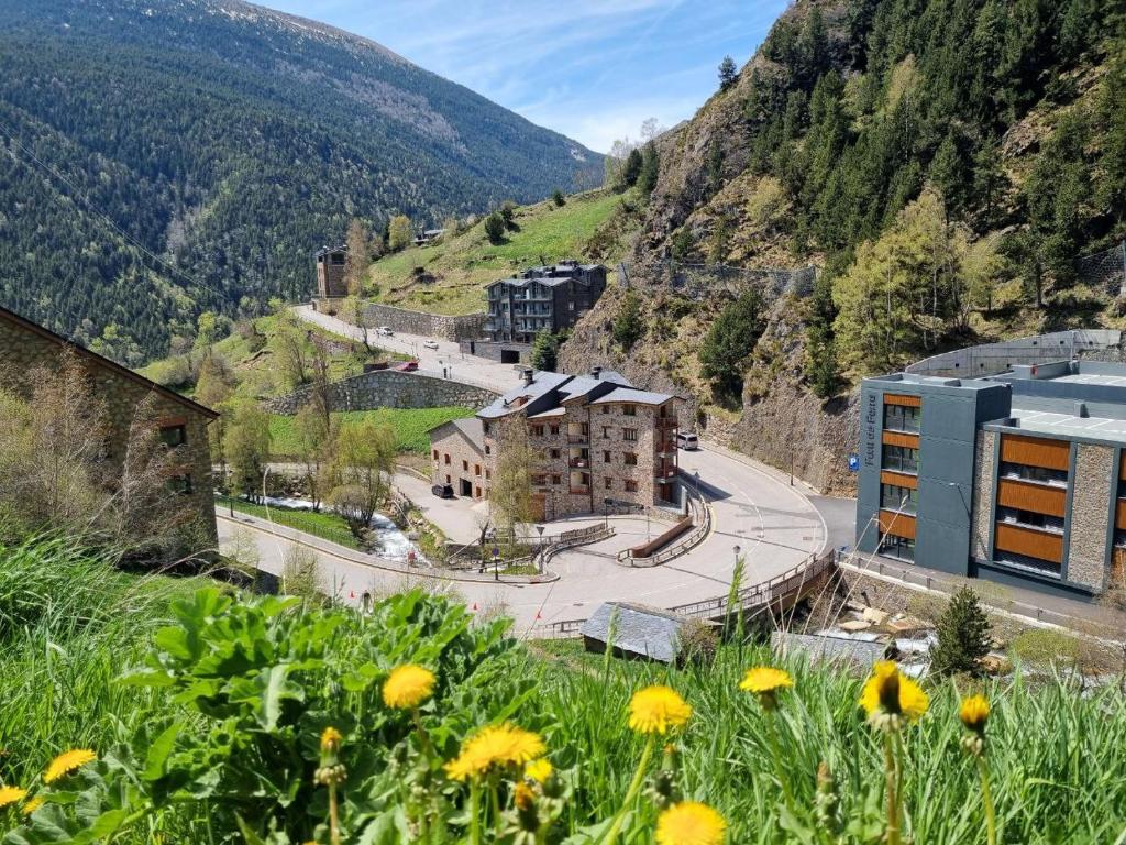 a building on a hill with yellow flowers in the foreground at Estudio encantador en el Río - 2Camas dobles SmartTV y WiFi in Canillo