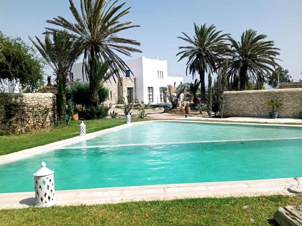 a swimming pool in the yard of a house with palm trees at La Maison d'Hélène Essaouira in Oulad el Madani