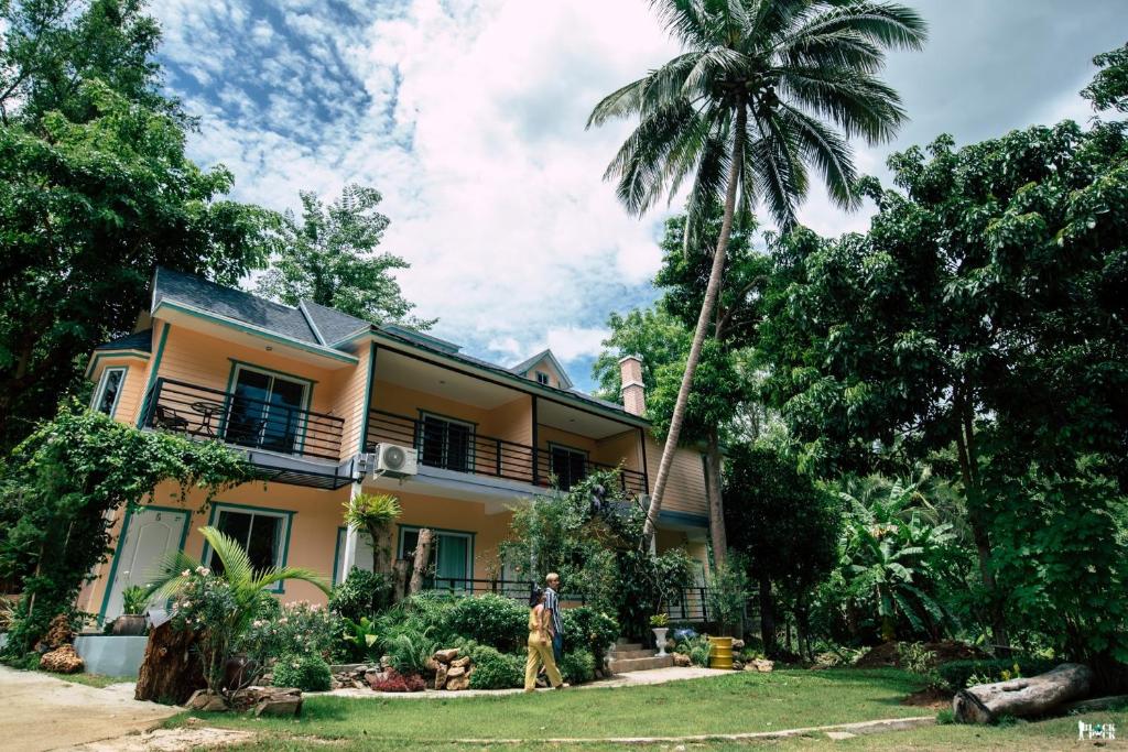 a man standing in front of a house with a palm tree at ชอว์ งาทอง รีสอร์ต Chor Ngar Thong Erawan in Kanchanaburi