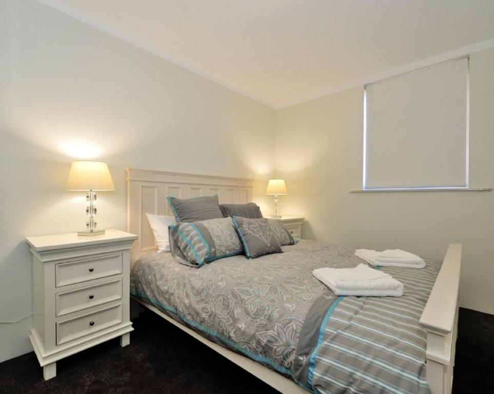 een slaapkamer met een bed met een nachtkastje en een raam bij Harbour Breeze - Central Fremantle Apartment in Fremantle