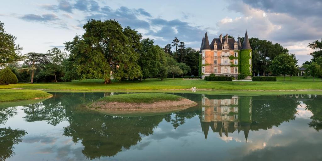 a large stone building with a lake and trees at Château D'Apigné Rennes in Le Rheu