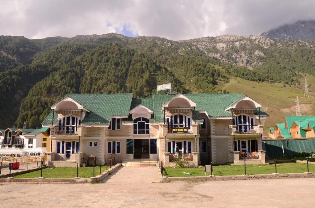 a large house with a green roof in front of a mountain at Hotel Mughal India in Sonāmarg
