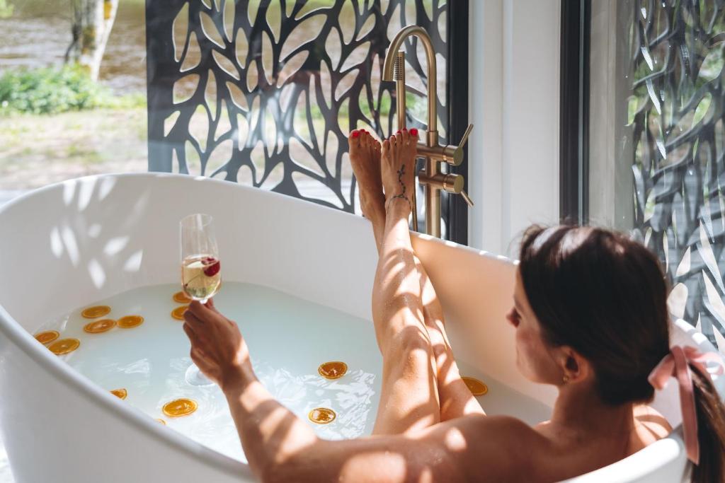 a woman sitting in a bath tub with a glass of wine at River Cabin in Inciems