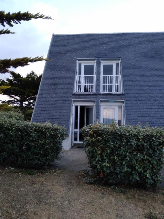 dom z niebieskim dachem, białymi oknami i krzewami w obiekcie Charmant logement Guidel Plage, chambre vue mer, piscine chauffée w mieście Guidel