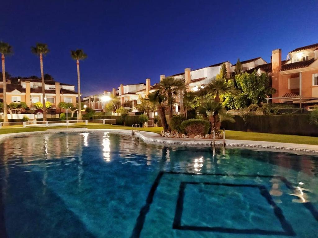una piscina notturna con palme e edifici di Adosado para familias al lado de la playa, con piscina a Castellón de la Plana