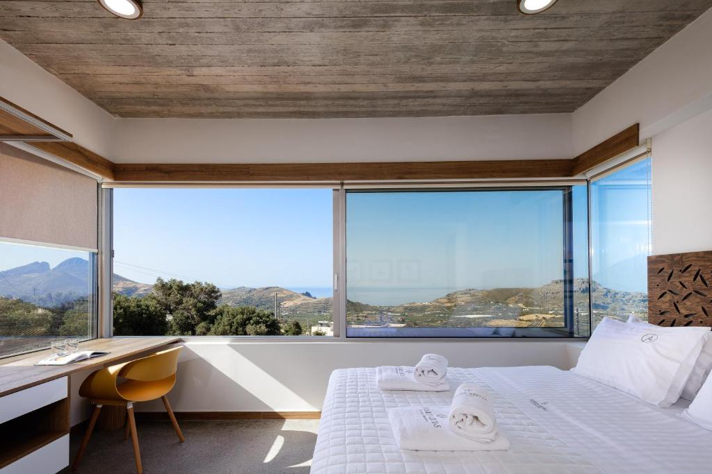 a bedroom with a bed and a desk and large windows at DOMUS AESTAS Luxury Residences in Plakias