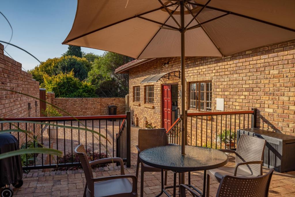 eine Terrasse mit einem Tisch, Stühlen und einem Sonnenschirm in der Unterkunft Bottle Brush Place WITH SOLAR in Roodepoort