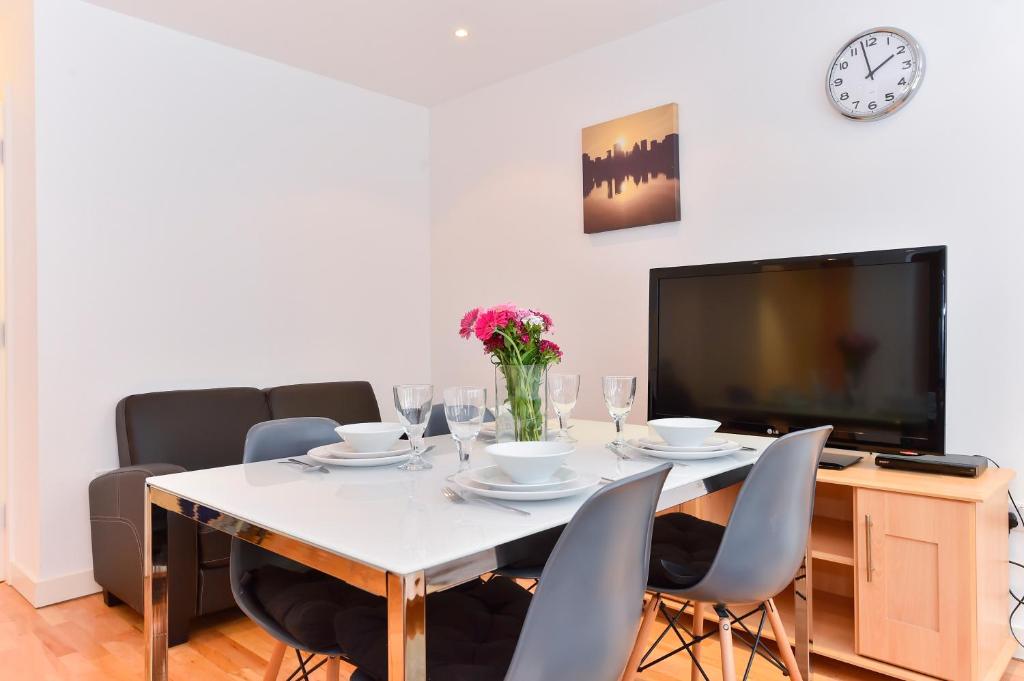 uma sala de jantar com uma mesa com cadeiras e uma televisão em Royal London Apartments em Londres
