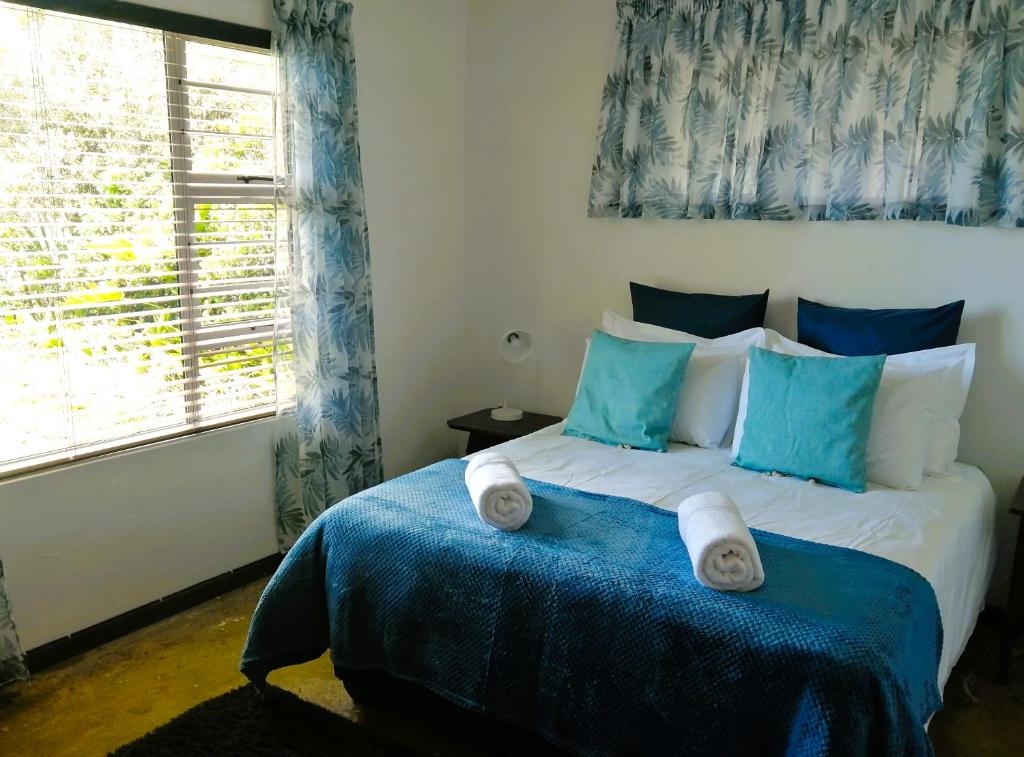 1 cama con almohadas azules y blancas y ventana en Come Stay No 6 - a well appointed two-bedroom unit with large covered patio en Gonubie Manor