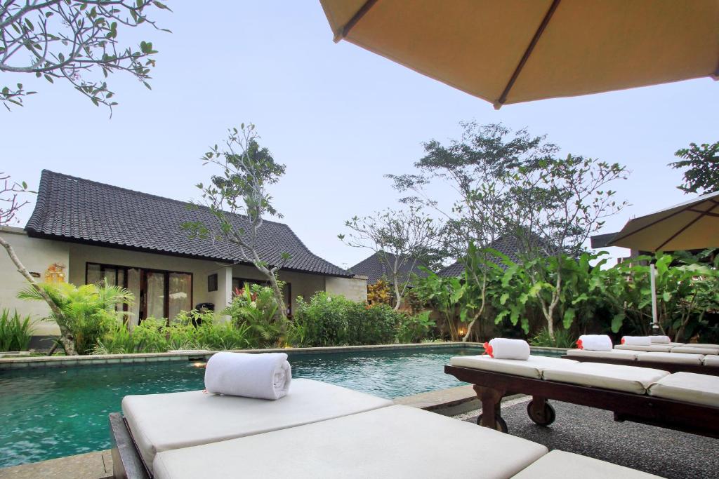 a swimming pool with chaise lounge chairs next to a house at Chili Ubud Cottage in Ubud