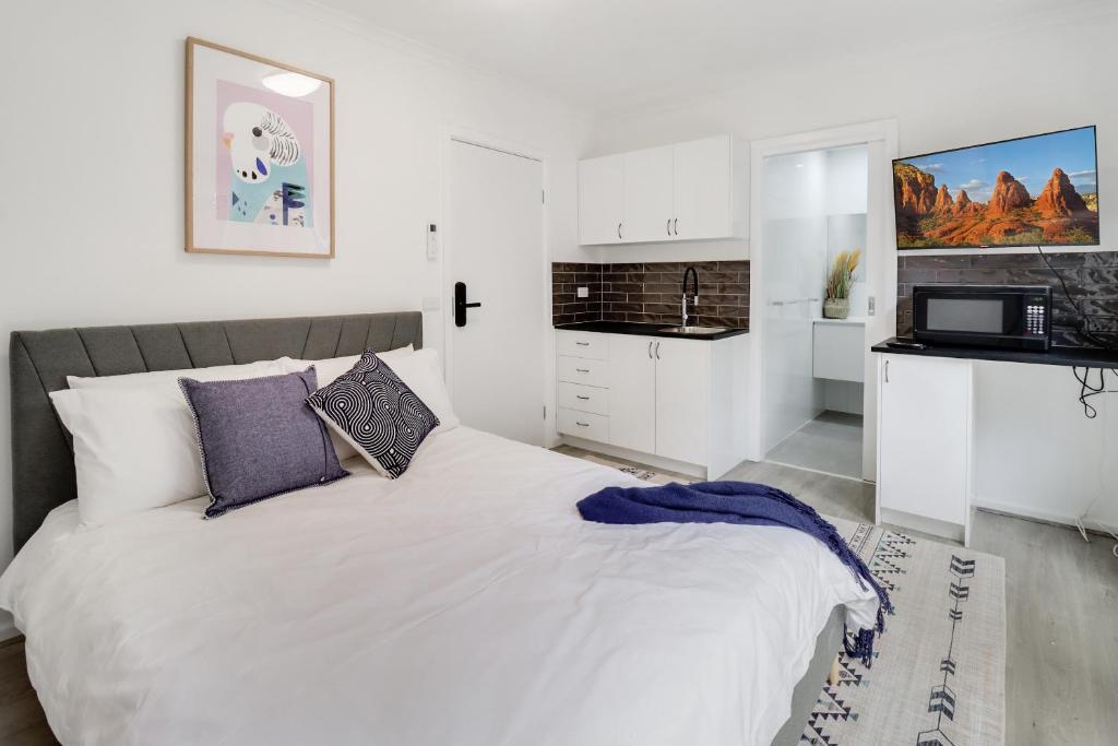Highton Accommodation (Geelong) في جيلونج: غرفة نوم بيضاء مع سرير ومطبخ