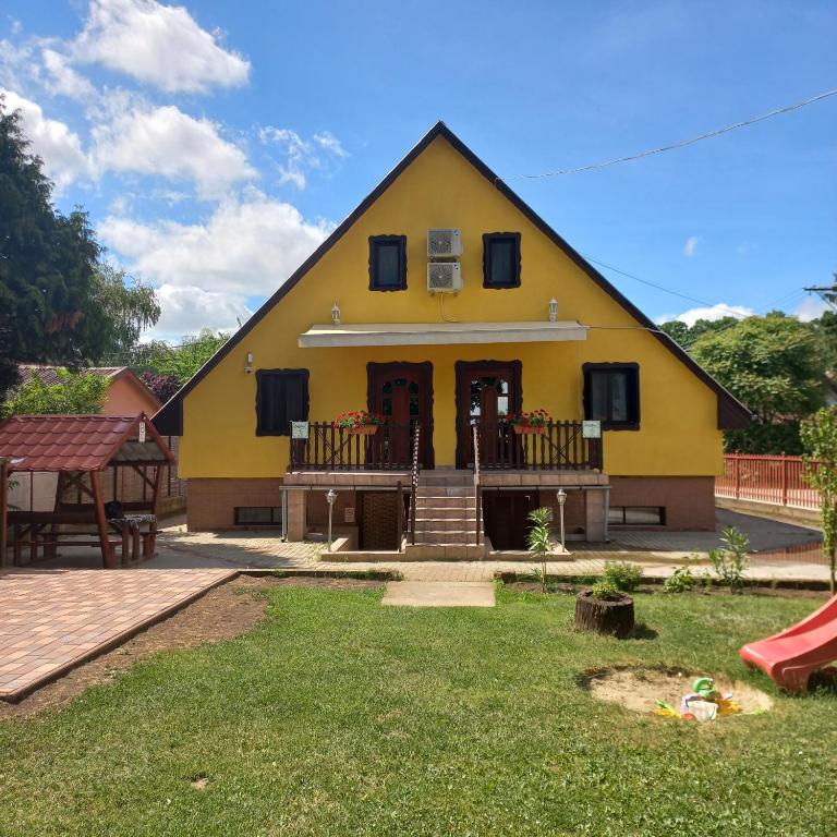 a yellow house with a porch and a playground at Krisztina Apartman 2-3 in Szigethalom