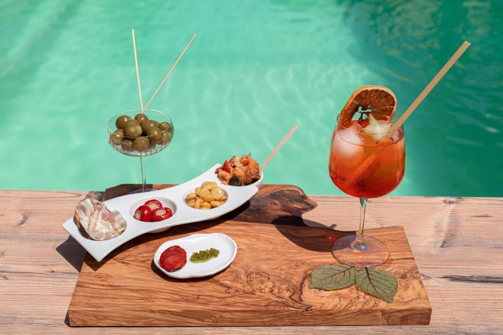 a drink and food on a wooden table next to a pool at Cala Cala Rooms,Restaurant & Farm Experience in Procida
