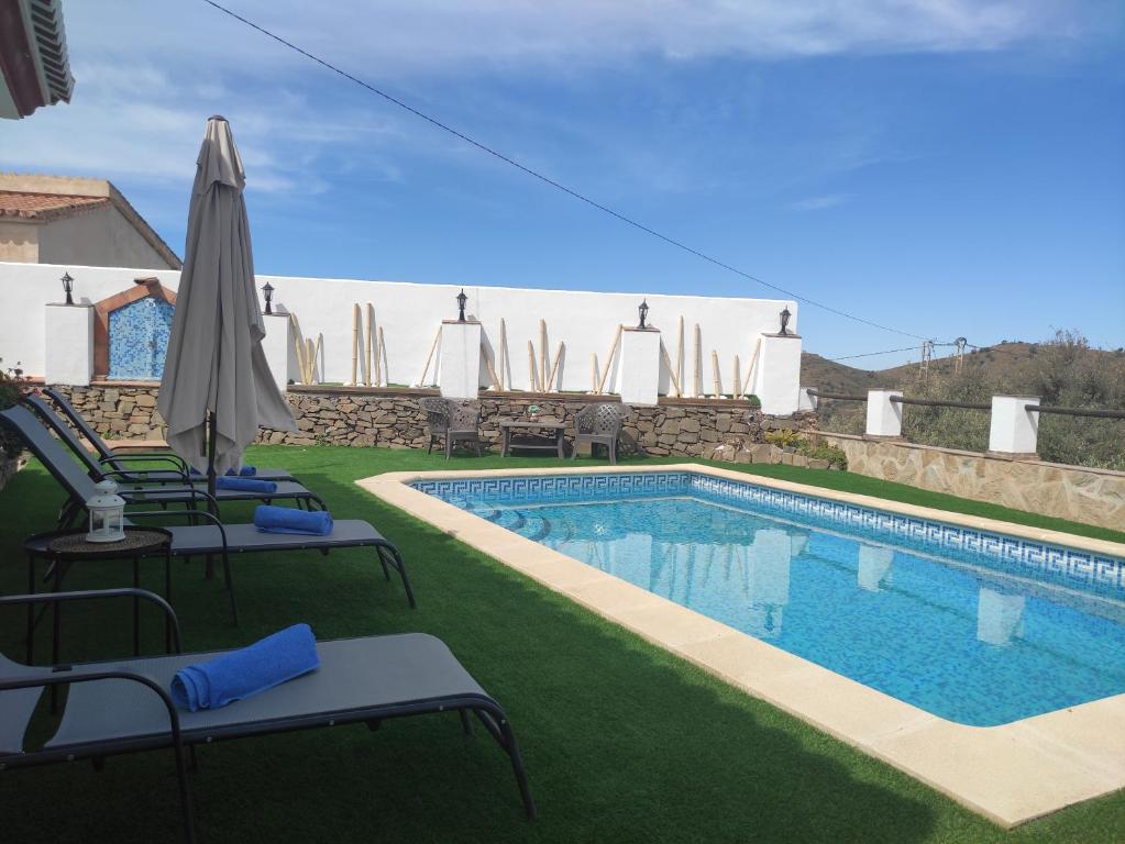 a swimming pool with lawn chairs and an umbrella at Casa rural Villa Miradri in Torrox