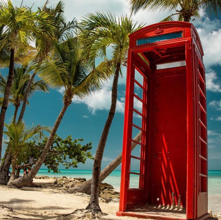 a red phone booth on a beach with palm trees at Petals Lovely Beach Villa in Saint Johnʼs