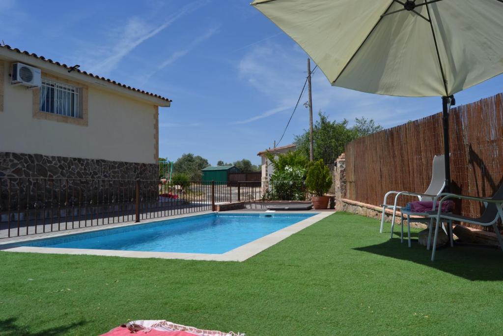 a swimming pool with an umbrella and a chair and a table at Casa Rural La Finca in Guadamur