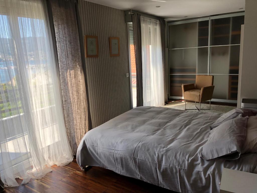 Un dormitorio con una cama y una silla y ventanas. en Casa Grila, en Pontevedra