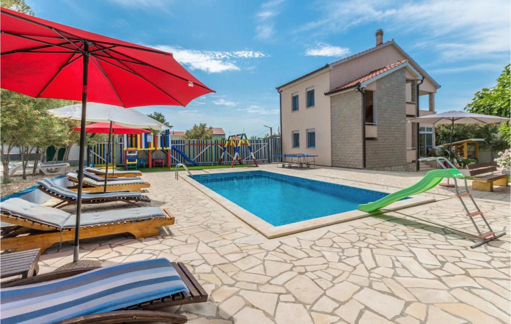a swimming pool with chairs and a red umbrella at Awesome Home In Kakma With Kitchen in Kakma