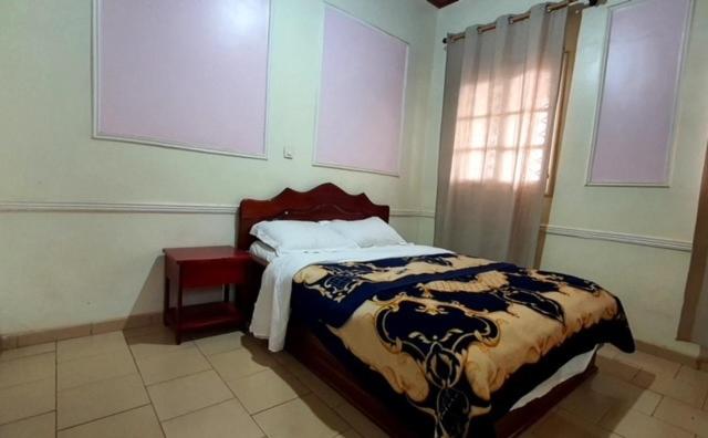 a bedroom with a bed and a table and a window at MANOIR DES PRINCESSES BAFOUSSAM in Bafoussam