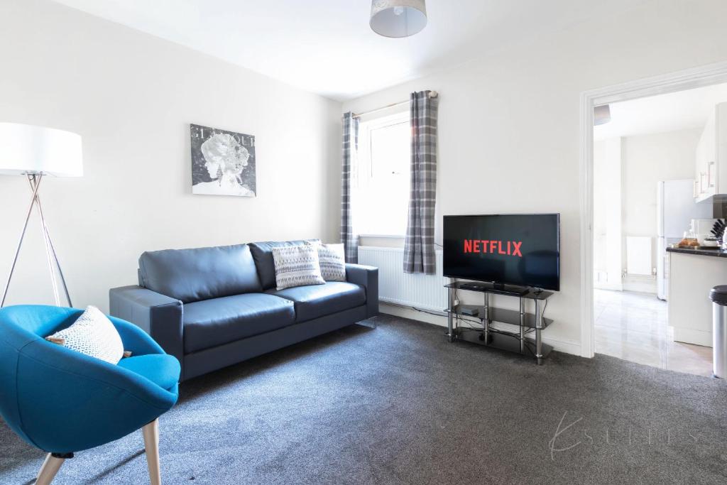 ein Wohnzimmer mit einem blauen Sofa und einem TV in der Unterkunft K Suites - Palmer Park - 4 Bedroom in Reading