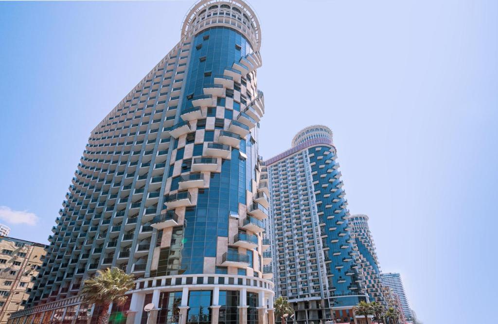 a tall blue building with palm trees in front of it at Apartment in Orbi Sea Tower in Batumi