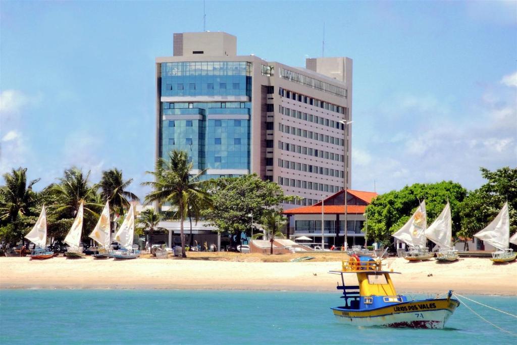 a boat in the water near a beach with a building at Best Western Premier Maceió in Maceió