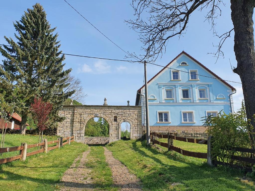 une maison bleue avec une arche dans une cour dans l'établissement Statek Bílý Dvůr, à Machov