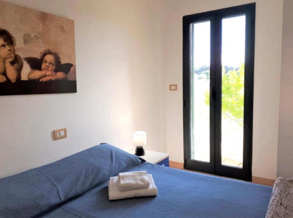 a bedroom with a bed with a blue blanket and a window at La Meta Sporting Rooms in Alghero