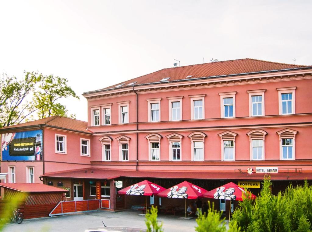 un gran edificio rosa con sombrillas rojas delante en Grand Hotel Jaroměř en Jaroměř