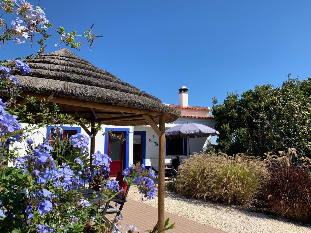 een huis met een rieten dak en een stoel en bloemen bij Quinta Samor in Aljezur